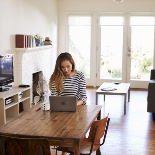 Woman Working From Home Using Laptop On Dining Table