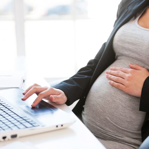 Pregnant woman working on laptop. Cropped image of pregnant businesswoman typing something on laptop while sitting at her working place in office